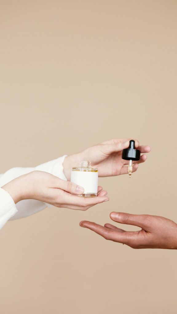 Minimalist photo of hands with a skincare dropper and bottle on a nude background.