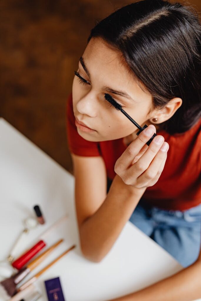 A young woman applies mascara, showcasing a makeup routine with cosmetics.